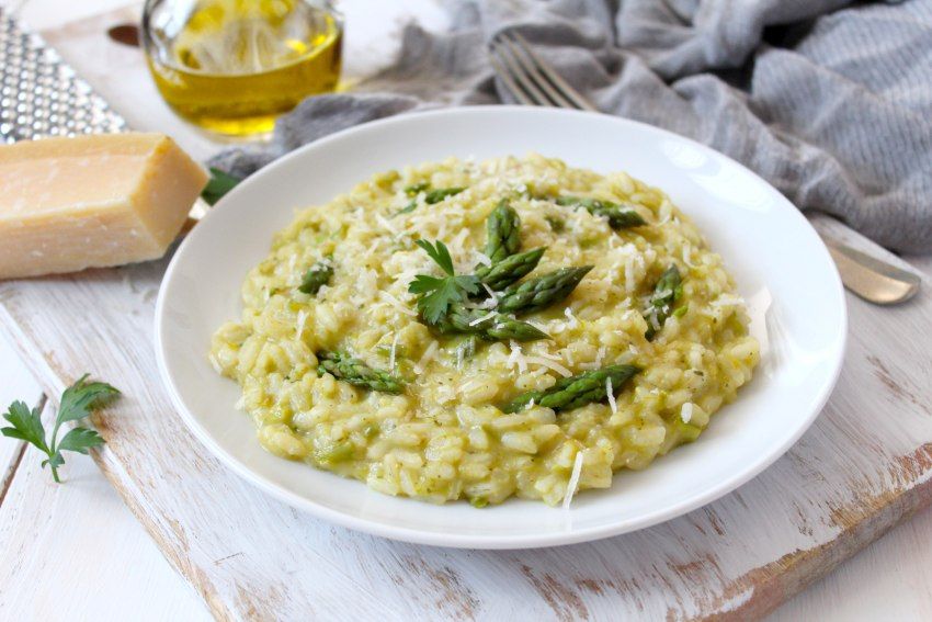 Teller Risotto mit grünem Spargel und geriebenem Parmesan auf einem Holzbrett