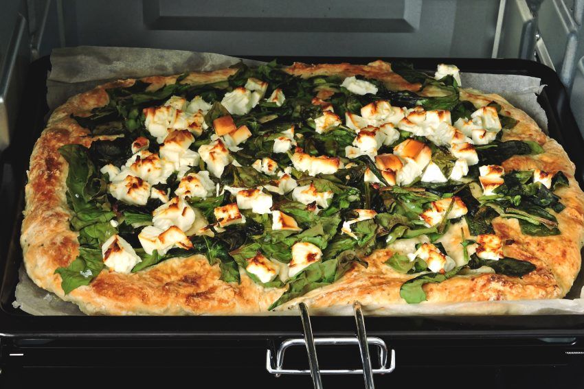Frisch gebackene Blechpizza mit Blattspinat und Feta auf einem Backblech