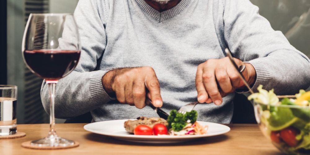 Mann isst am gedeckten Tisch ein Abendessen mit Salat