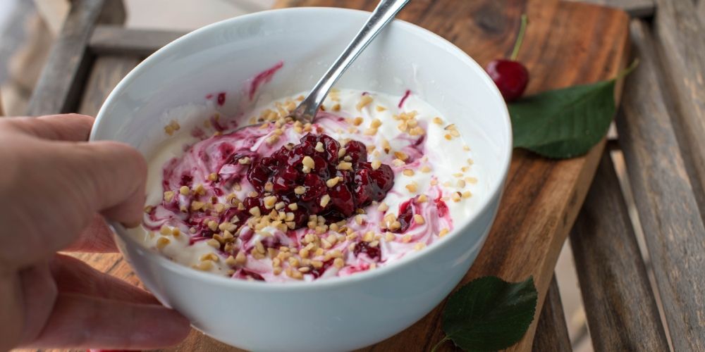 Schüssel Joghurt mit Kirschen und gehackten Nüssen auf einem Holztisch