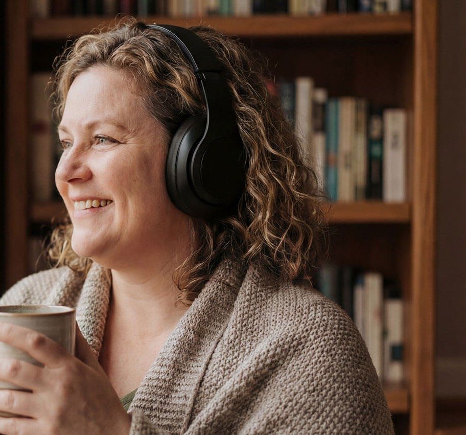 Frau mit Kopfhörern und einer Tasse hört einen Podcast